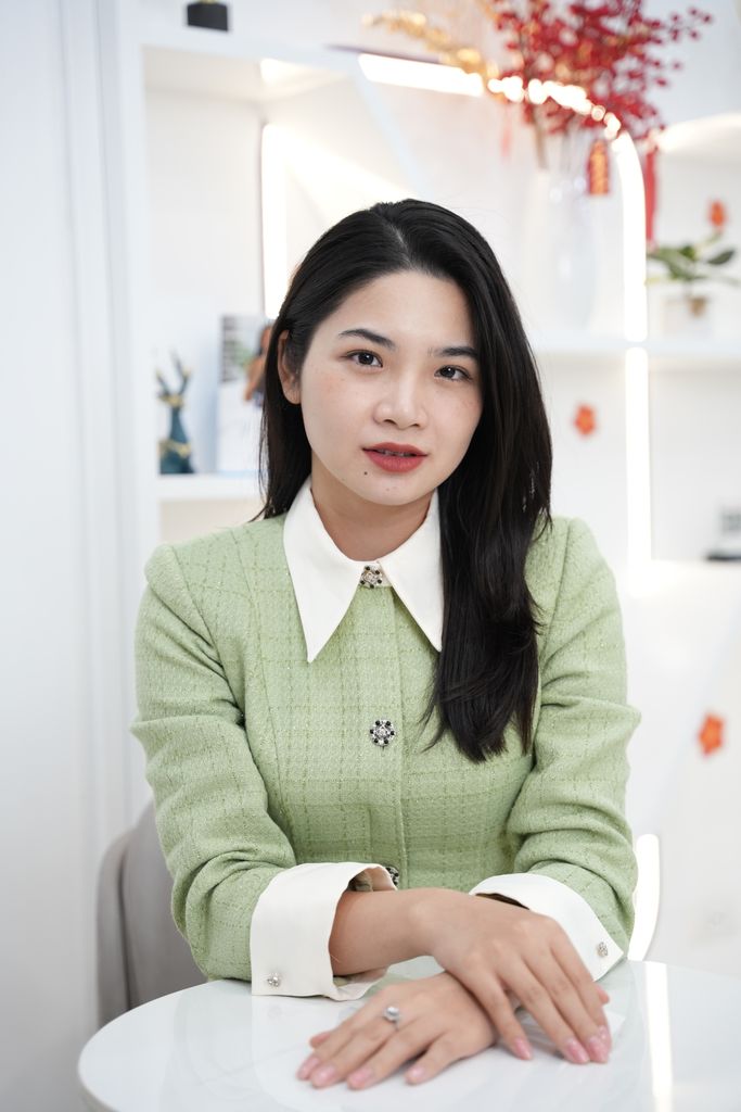 Young woman in a green jacket posing indoors at a white table.